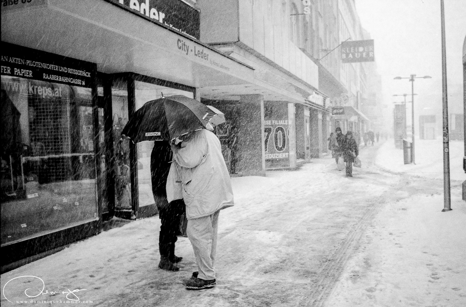 Zwei Menschen sch&uuml;tzen sich mit einem Schirm im Schneegest&ouml;ber in Wien von Fotograf Dominique Hammer