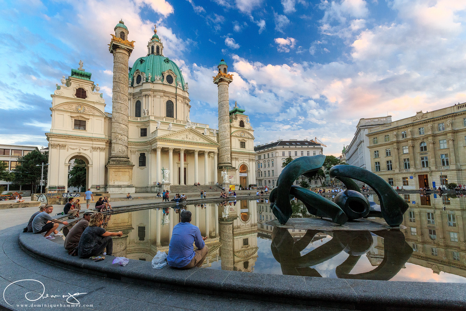 Menschen sitzen am Brunnen vor der Karlskirche von Fotograf Dominique Hammer